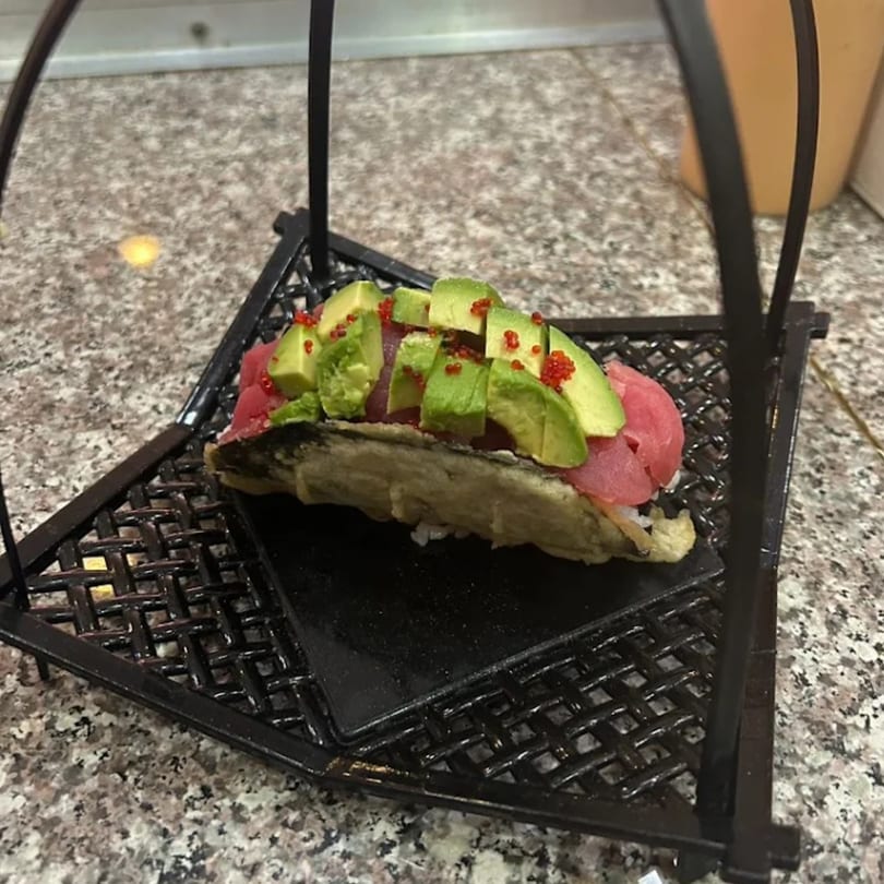 Tuna and avocado sushi taco with red roe, served on a black metal stand.