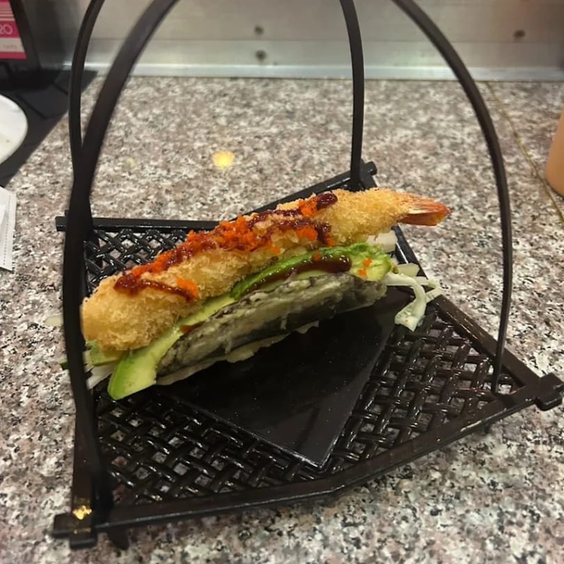 Tempura shrimp sushi roll with avocado and sauce, served in a black metal basket.