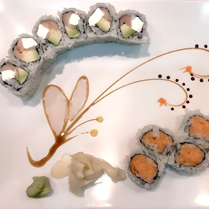Two types of sushi rolls, one with cream cheese and avocado, the other with orange filling, on a white plate with artistic sauce drizzles.
