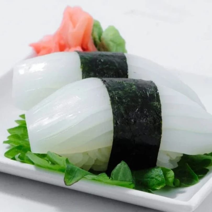 Two pieces of squid nigiri sushi with seaweed, ginger, and wasabi on a white plate.