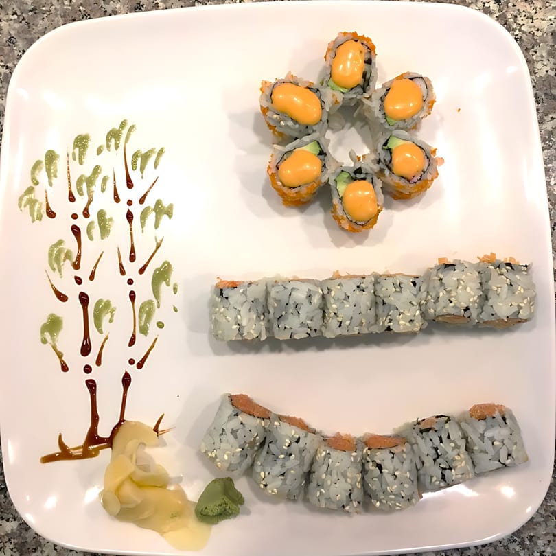 A white plate with three types of sushi rolls, ginger, wasabi, and decorative sauce drizzles.